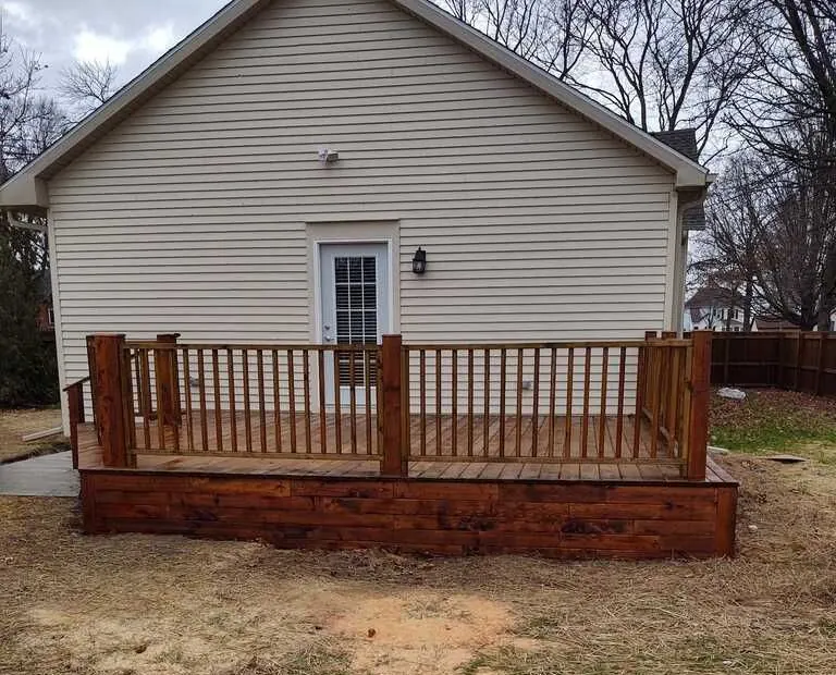 New backyard deck with stained horizontal skirting and railings along the back of a sided home